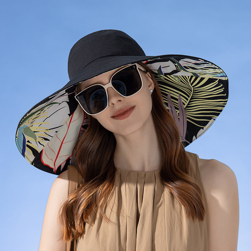Woman wearing a black sun hat with a colorful leaf pattern against a clear blue sky.