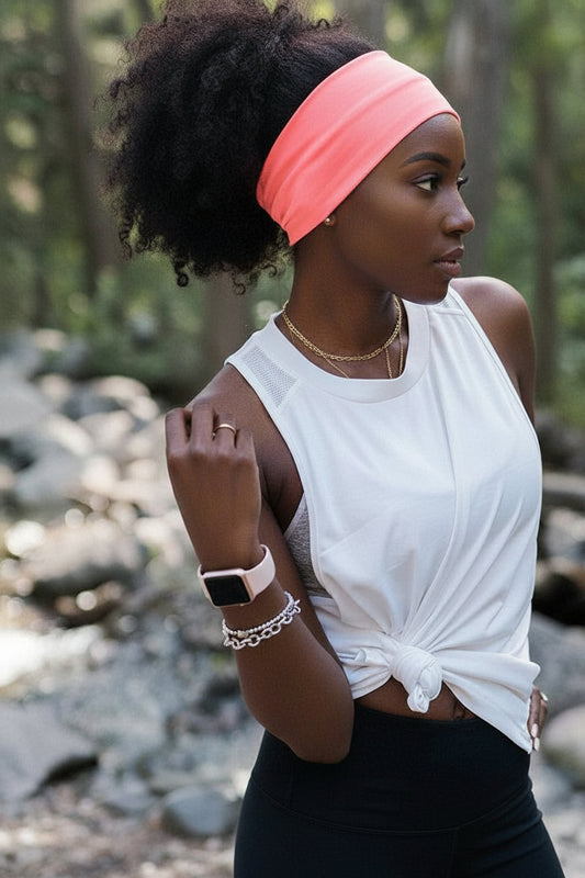 Woman wearing a white sleeveless top and black leggings with a pink headband in a natural setting.