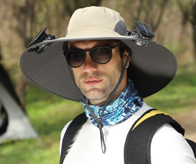 Man wearing a large sun hat with solar battery and fans, outdoors.