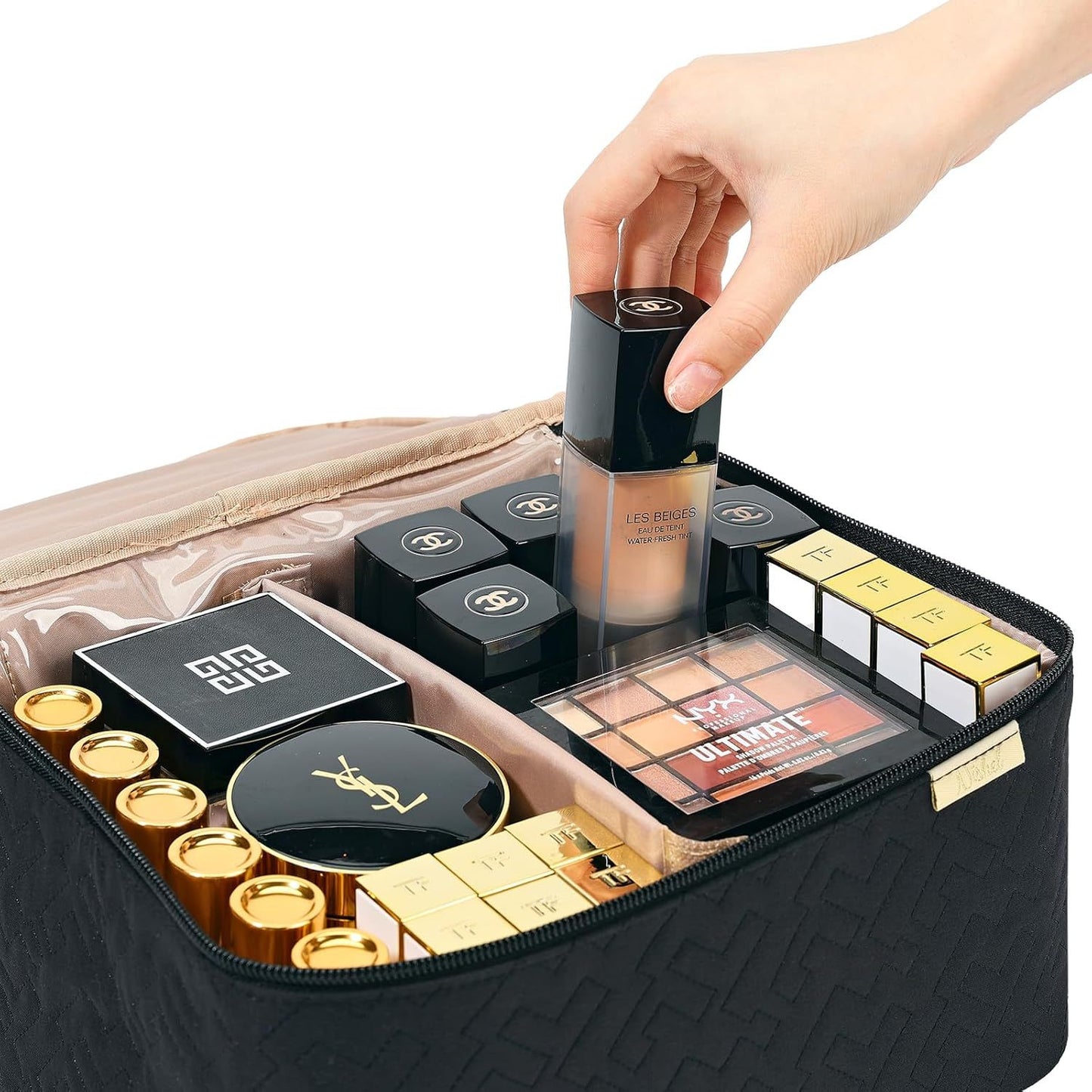 Makeup products in a black cosmetic bag with a hand reaching in to pick up a product.
