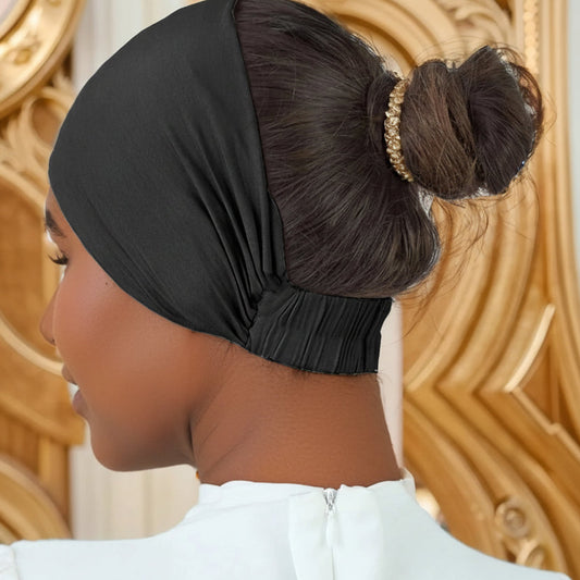 Woman wearing a black headscarf with a gold hair accessory against a decorative wall.