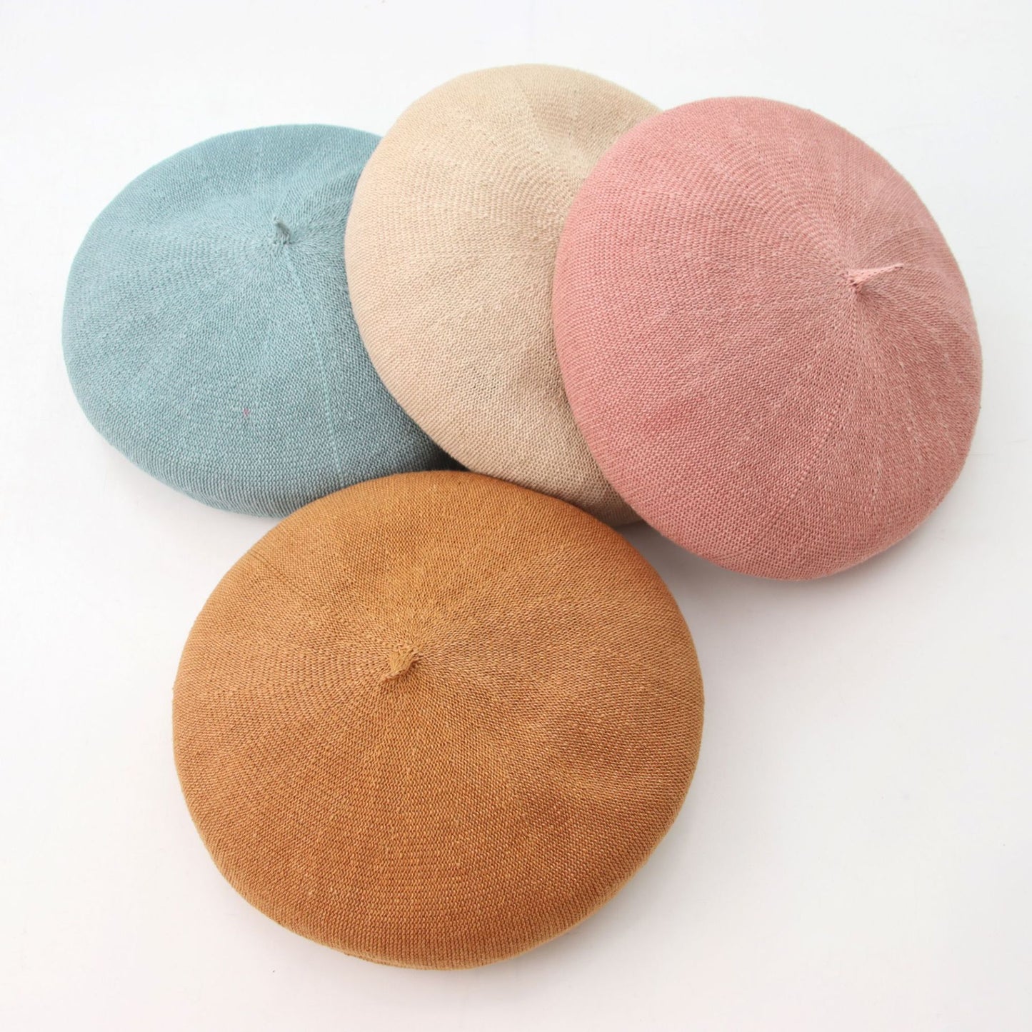 Four colorful berets (blue, beige, pink, and brown) on a white background