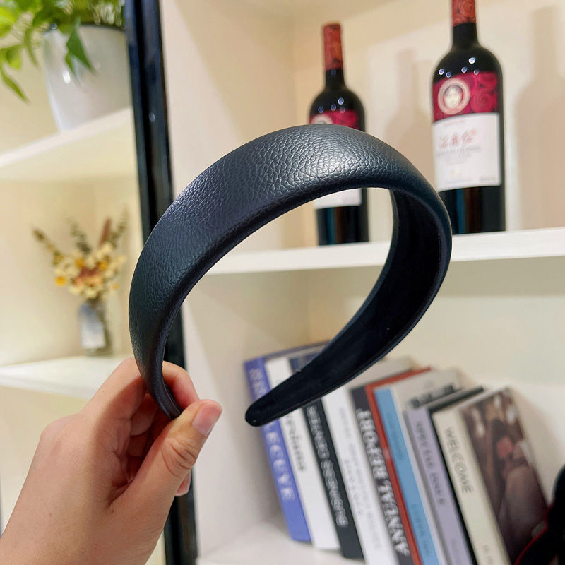 Black headband held in front of a bookshelf with wine bottles and books.