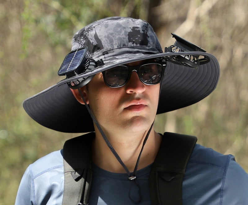 Person wearing a large sun hat with solar panel and fans, outdoors.