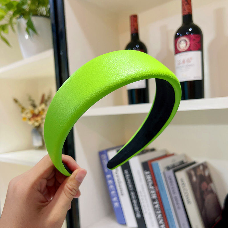 Green headband held in front of a bookshelf with wine bottles and books.
